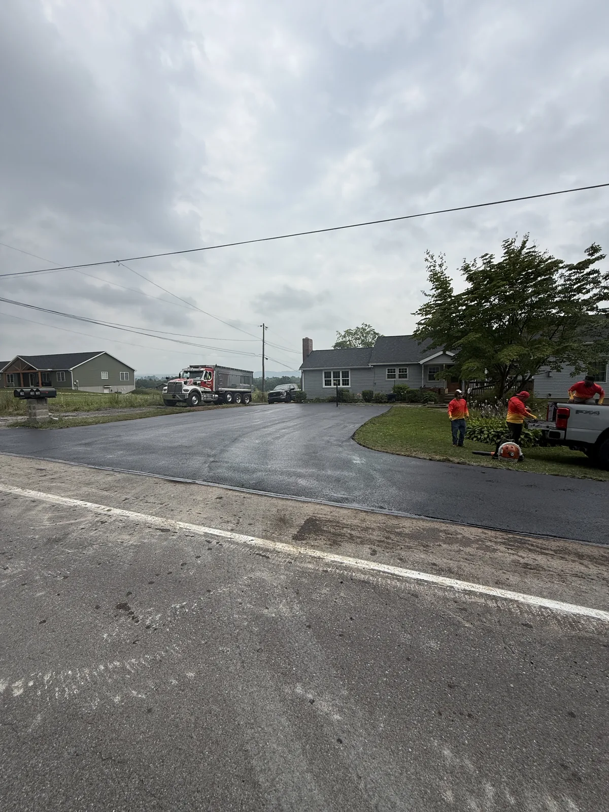 Fresh asphalt driveway meeting an existing roadway in front of a home