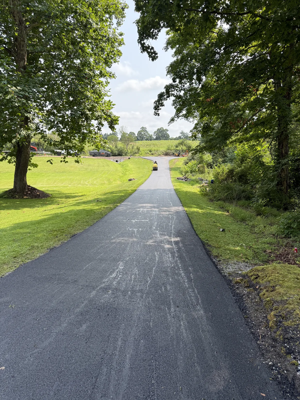 Roller on a paved driveway between lawns and trees.