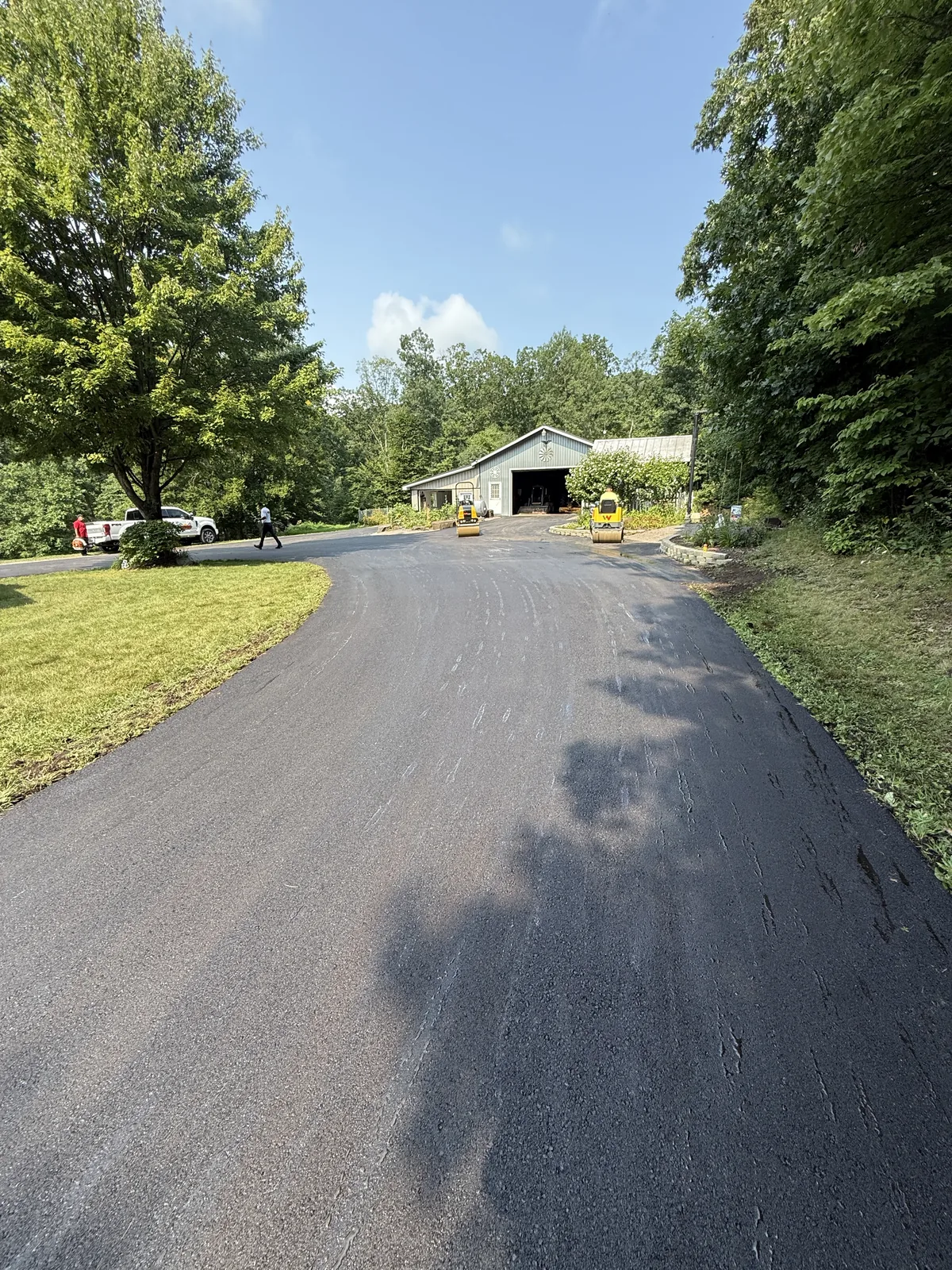 Asphalt driveway leading toward a building with two rollers beside the entrance.