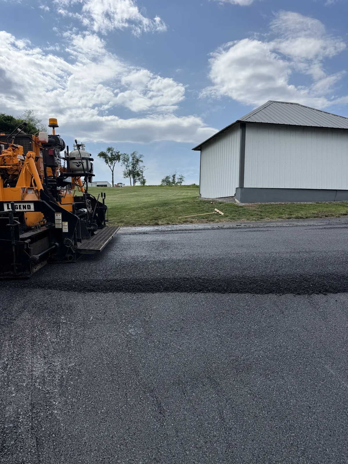 Asphalt paving equipment beside a newly placed driveway surface