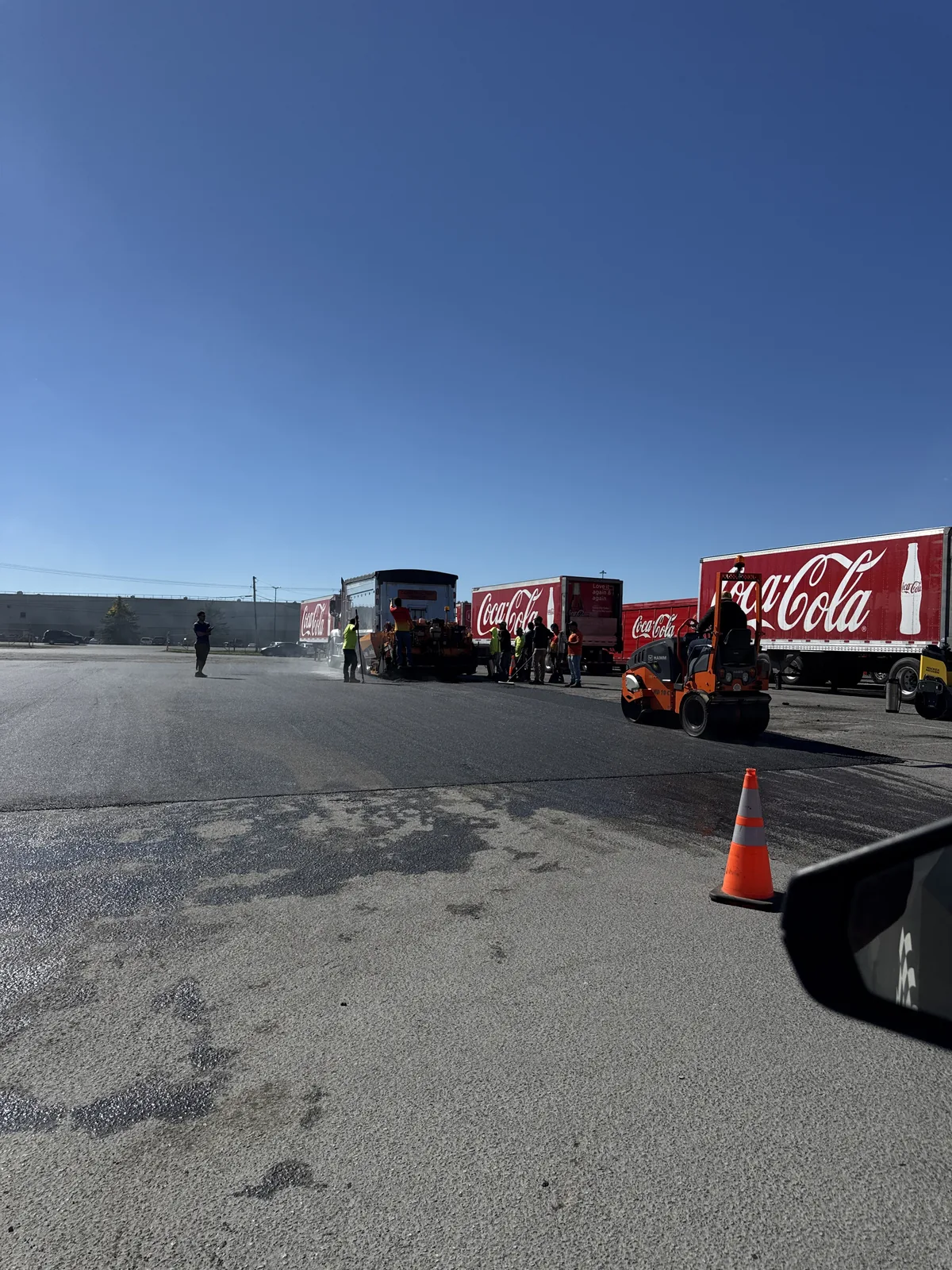 Commercial-yard pavement with a traffic cone and parked trucks along the side.