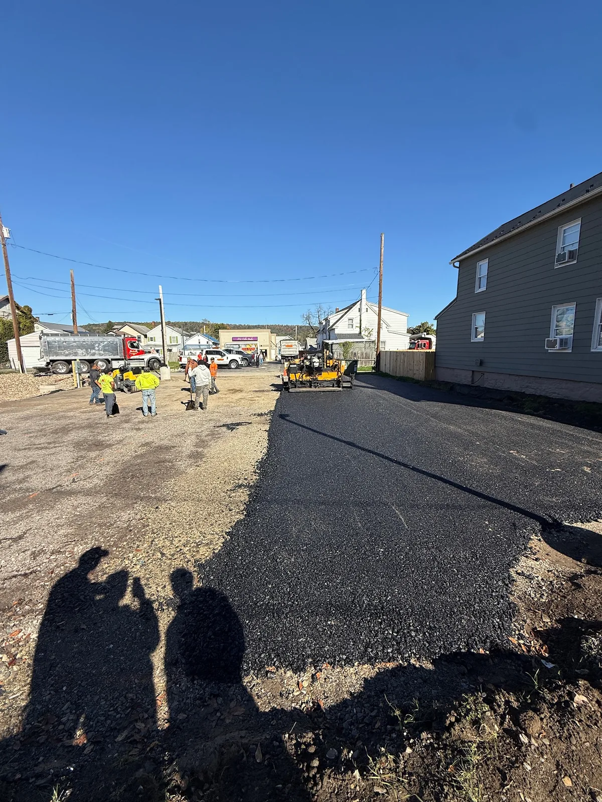Asphalt work in progress beside an unpaved portion of a parking area.