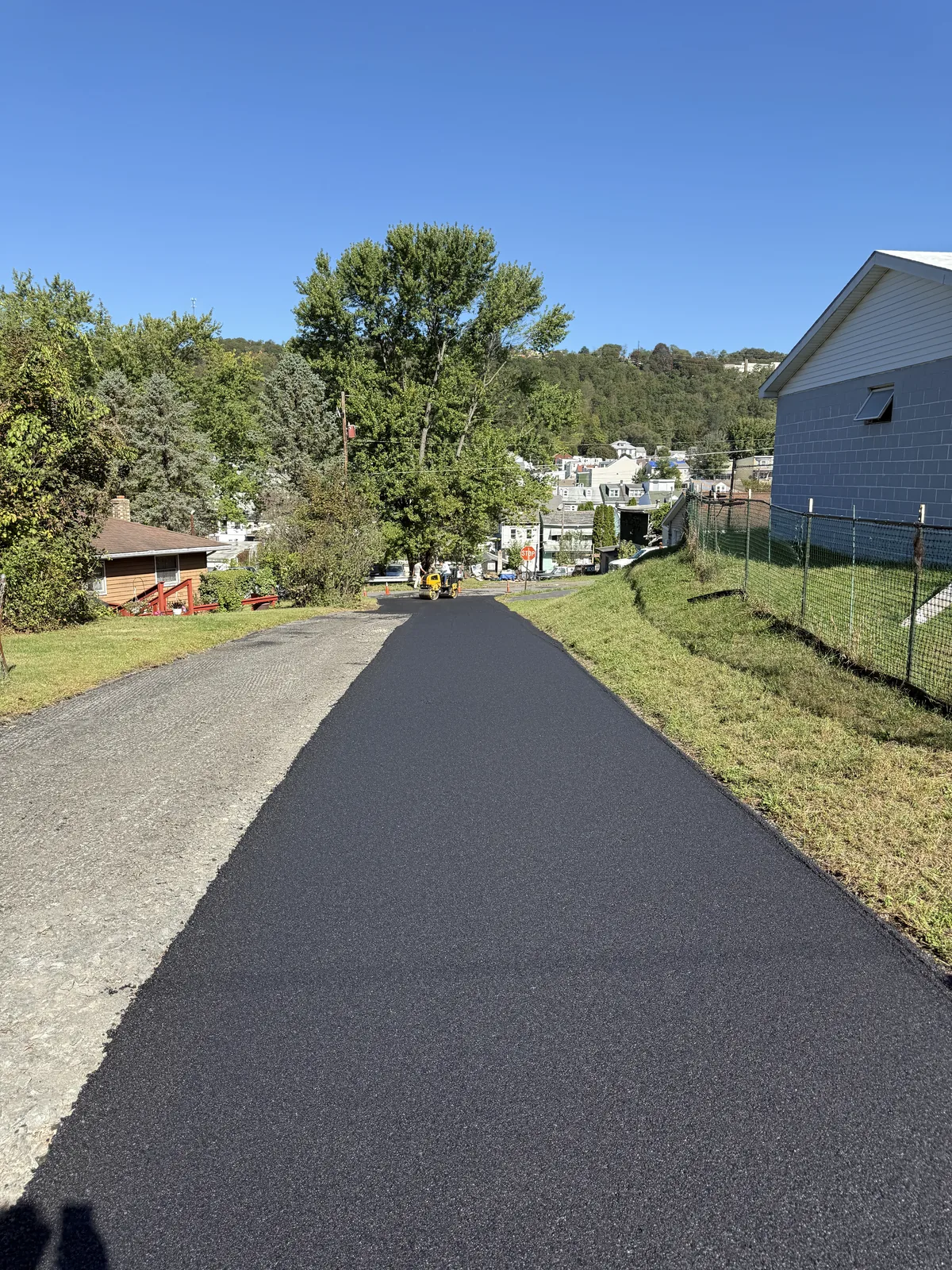 Fresh asphalt lane beside an older roadway surface with a roller near the intersection.