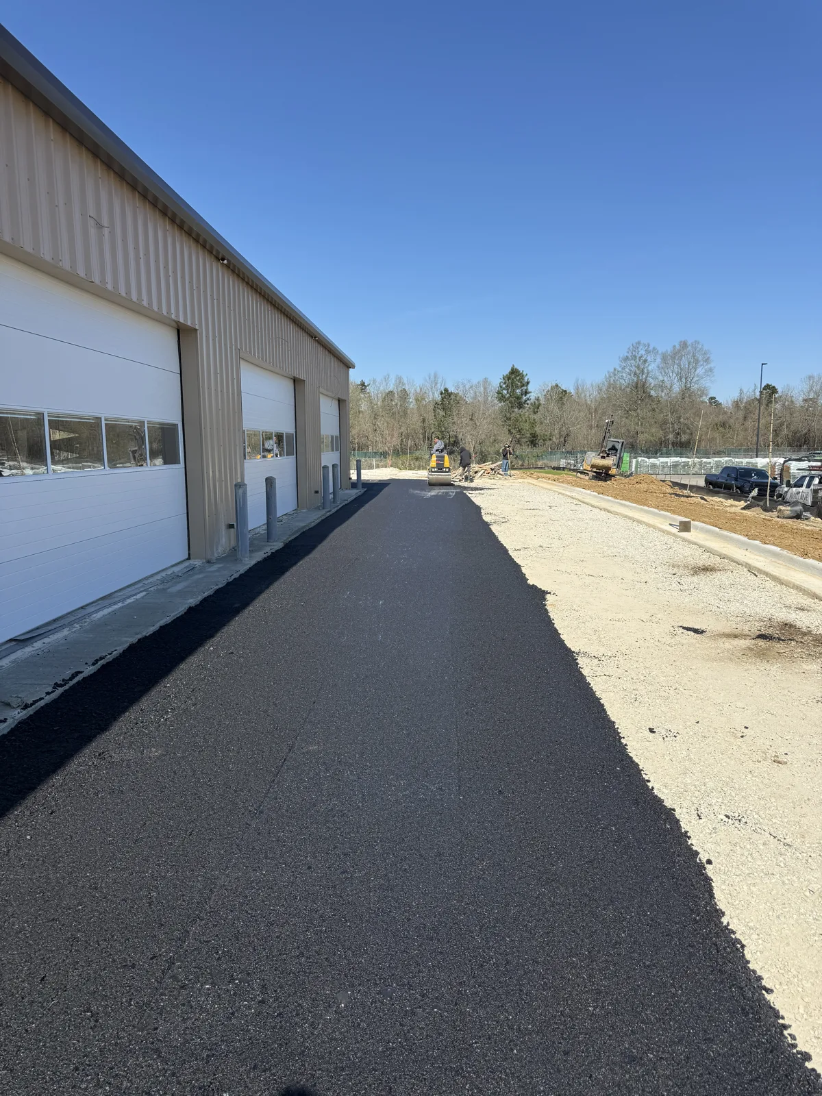 Fresh asphalt along a commercial building, with defined edges beside the adjoining ground.