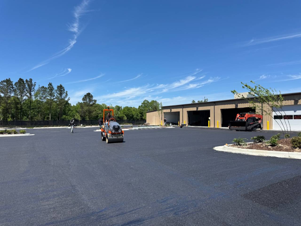 Fresh asphalt in front of the Caliber Collision building in Denham Springs, Louisiana, with paving equipment on site.