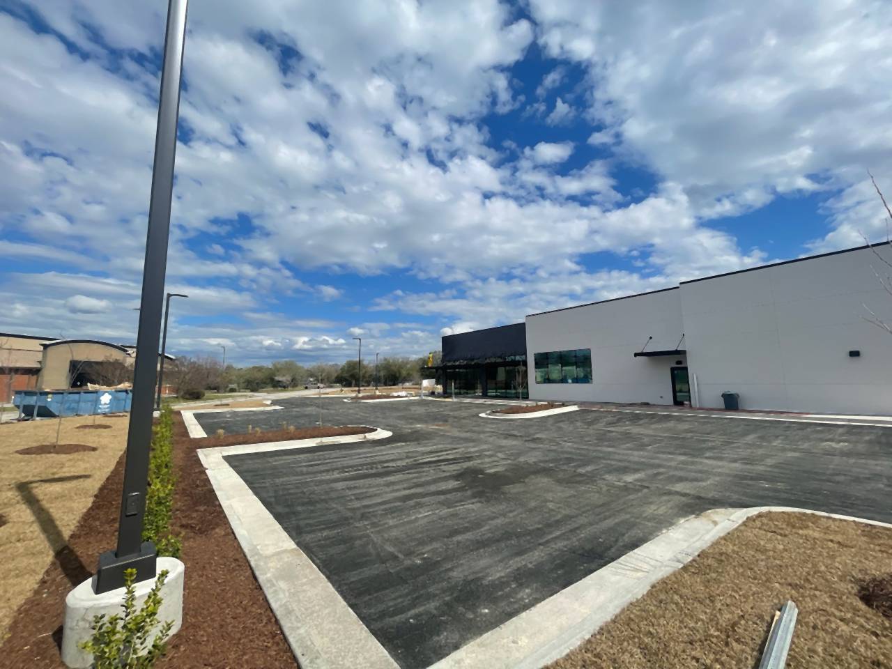 Freshly paved commercial lot with concrete curbs and a light pole.