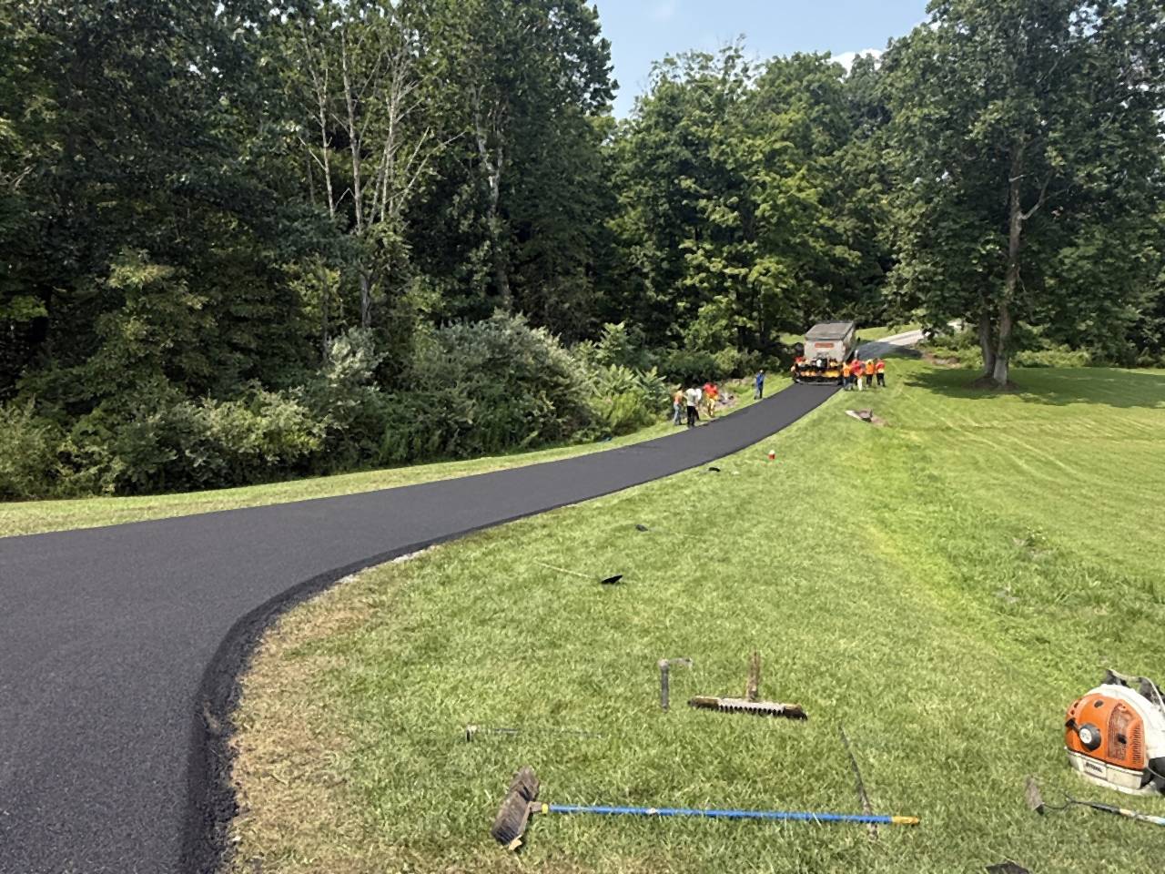 Fresh asphalt driveway curving past a lawn and trees.