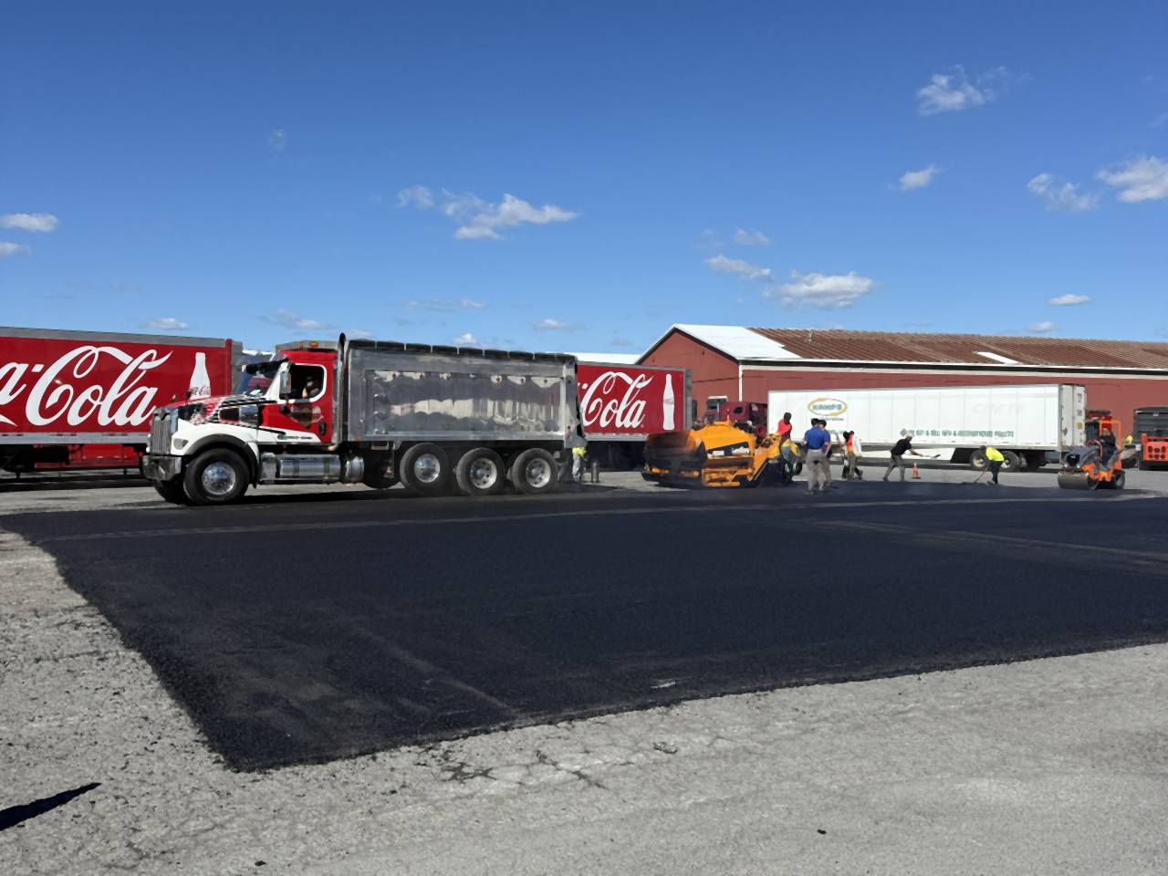 New asphalt across a truck yard after milling, with trailers in the background.
